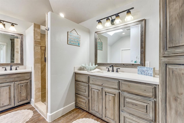 bathroom featuring wood finished floors, tiled shower, two vanities, and a sink