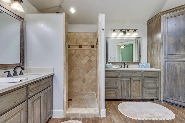 bathroom featuring two vanities, tiled shower, a sink, and wood finished floors