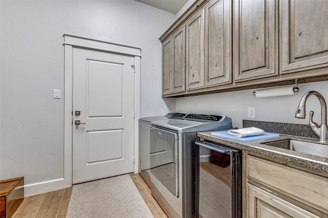 clothes washing area with a sink, baseboards, light wood-style floors, cabinet space, and washing machine and clothes dryer