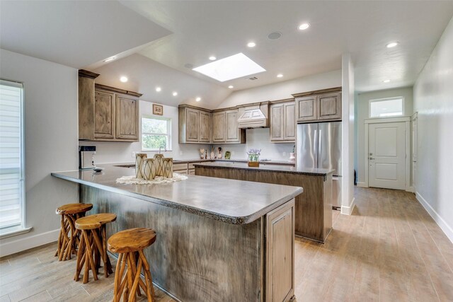 kitchen featuring a center island, custom exhaust hood, light wood-style flooring, a peninsula, and stainless steel refrigerator