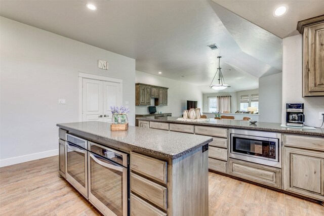 kitchen with stainless steel appliances, a kitchen island, light wood-style flooring, and baseboards