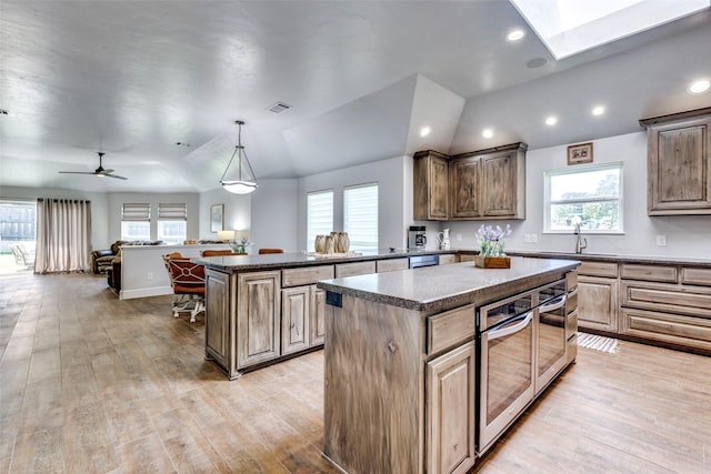 kitchen featuring a sink, a kitchen island, visible vents, light wood-type flooring, and dark countertops