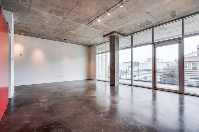 empty room with finished concrete floors, floor to ceiling windows, and baseboards