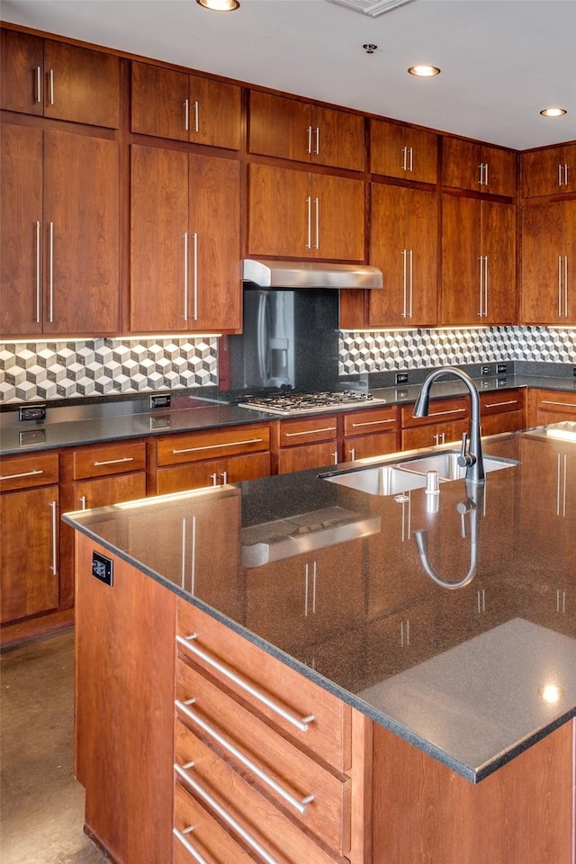 kitchen featuring decorative backsplash, brown cabinets, under cabinet range hood, stainless steel gas cooktop, and a sink