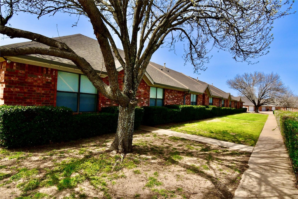 view of property exterior featuring a yard, roof with shingles, and brick siding