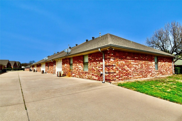 view of property exterior featuring a shingled roof, concrete driveway, and brick siding