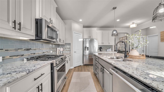 kitchen with light wood finished floors, white cabinets, decorative light fixtures, stainless steel appliances, and a sink