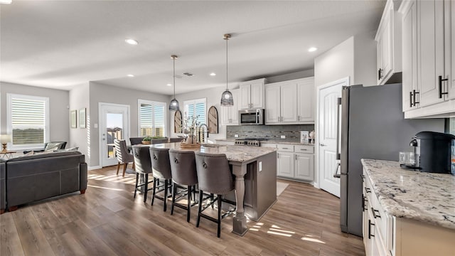 kitchen with white cabinets, open floor plan, a kitchen breakfast bar, decorative backsplash, and stainless steel microwave