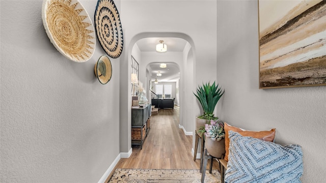 corridor with light wood-style floors, baseboards, and arched walkways