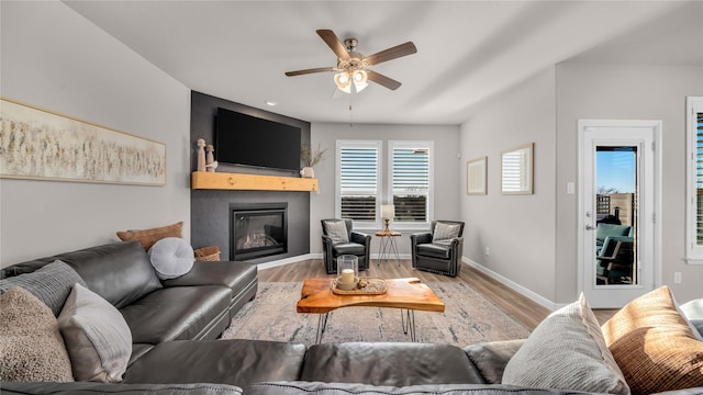 living area featuring ceiling fan, baseboards, wood finished floors, and a glass covered fireplace