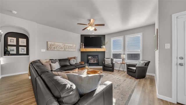 living room with a large fireplace, ceiling fan, wood finished floors, and baseboards