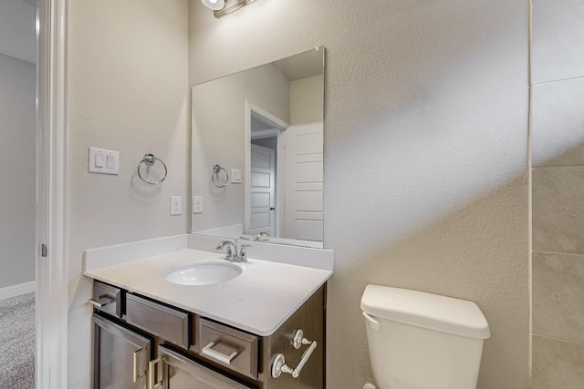 half bath featuring a textured wall, vanity, and toilet