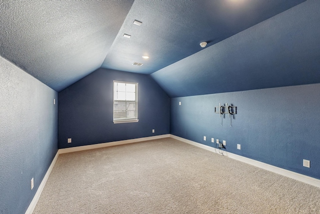 additional living space featuring visible vents, a textured wall, vaulted ceiling, a textured ceiling, and carpet flooring