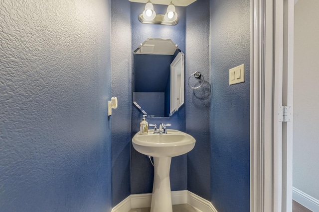 half bathroom featuring a textured wall and baseboards