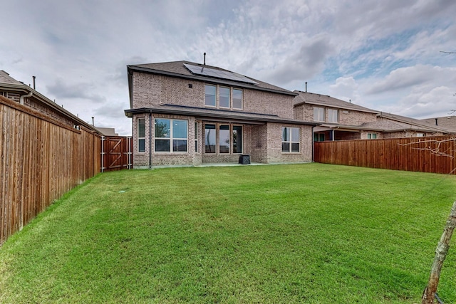 rear view of house featuring a yard, roof mounted solar panels, a fenced backyard, and brick siding