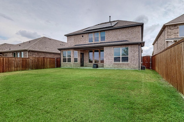 back of house with brick siding, solar panels, a lawn, a patio area, and a fenced backyard