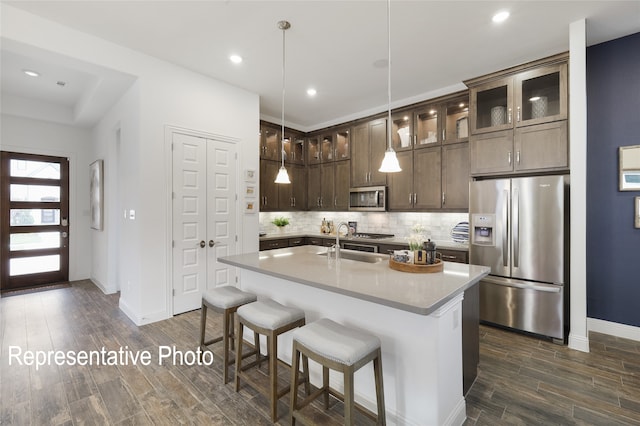 kitchen with dark brown cabinetry, wood finish floors, a sink, appliances with stainless steel finishes, and backsplash