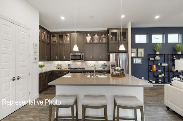 kitchen featuring stainless steel appliances, open floor plan, a sink, dark brown cabinetry, and a kitchen breakfast bar