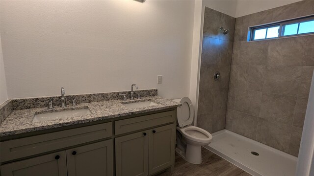 bathroom featuring toilet, a tile shower, a sink, and wood finished floors