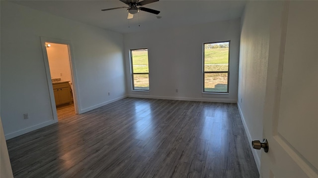 unfurnished bedroom with dark wood-style floors, ceiling fan, baseboards, and connected bathroom