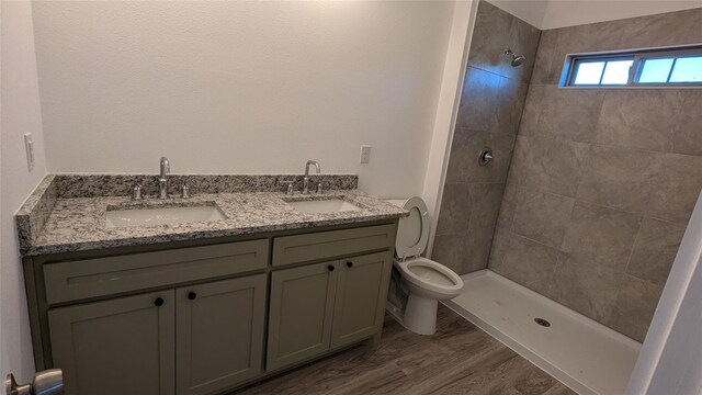 full bath with a tile shower, double vanity, a sink, and toilet