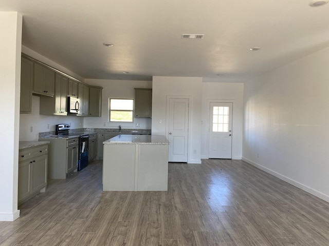 kitchen with white microwave, electric range, wood finished floors, visible vents, and a center island