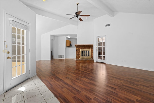 unfurnished living room featuring a brick fireplace, visible vents, vaulted ceiling with beams, and ceiling fan