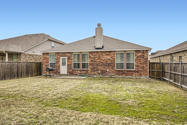 back of property with a fenced backyard, a chimney, a lawn, and brick siding