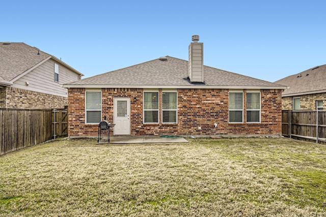 back of property with a fenced backyard, a yard, a chimney, and brick siding