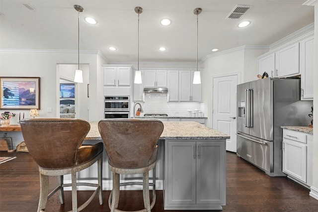 kitchen with visible vents, ornamental molding, dark wood-type flooring, stainless steel appliances, and under cabinet range hood