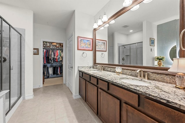 full bath with double vanity, a stall shower, tile patterned floors, a walk in closet, and a sink