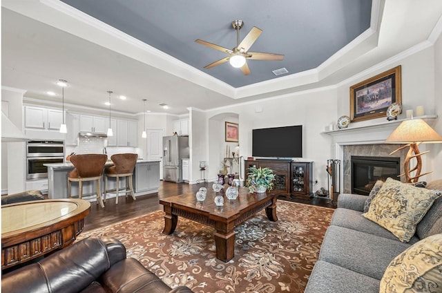 living room with arched walkways, a premium fireplace, visible vents, a tray ceiling, and dark wood finished floors