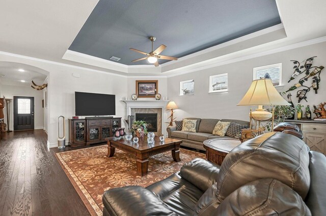 living room with a tray ceiling, arched walkways, wood-type flooring, visible vents, and a tile fireplace