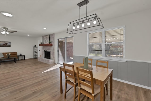 dining room featuring wood finished floors, recessed lighting, ceiling fan, wainscoting, and a large fireplace