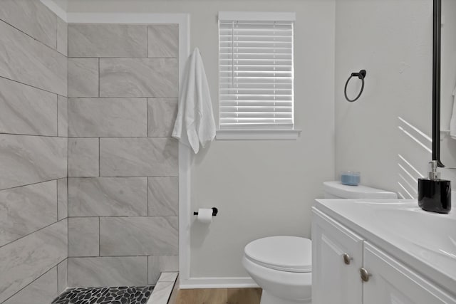 bathroom featuring vanity, wood finished floors, baseboards, tiled shower, and toilet