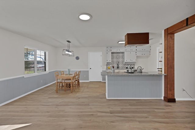 kitchen featuring light wood finished floors, wainscoting, a peninsula, hanging light fixtures, and white cabinetry