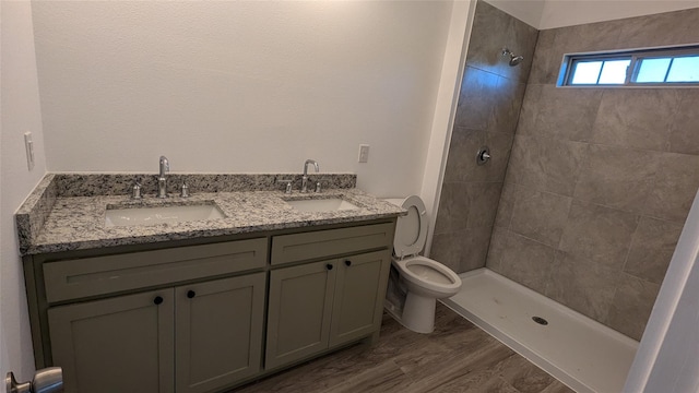 full bath with toilet, double vanity, a tile shower, and a sink