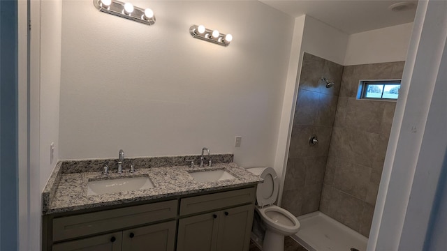 full bathroom with a tile shower, double vanity, a sink, and toilet