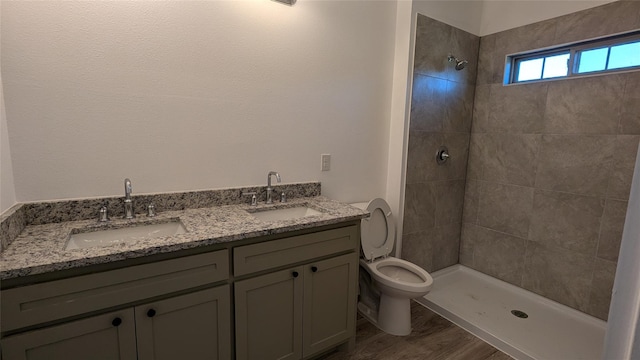 full bathroom featuring a tile shower, wood finished floors, a sink, and toilet