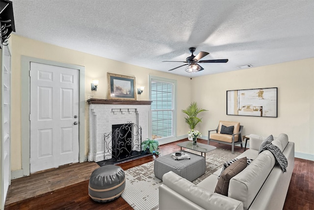 living room featuring a textured ceiling, wood finished floors, visible vents, a ceiling fan, and a brick fireplace