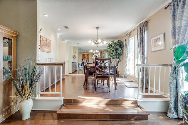 dining space with baseboards, visible vents, wood finished floors, stairs, and a notable chandelier