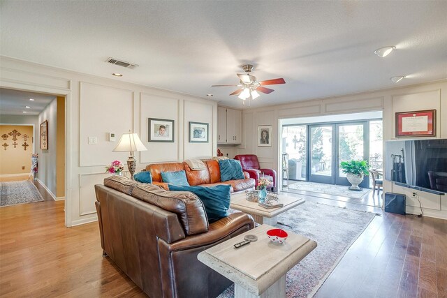 living area with a ceiling fan, light wood-type flooring, visible vents, and a decorative wall