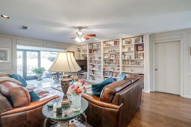 living room featuring visible vents, a decorative wall, a ceiling fan, a textured ceiling, and wood finished floors