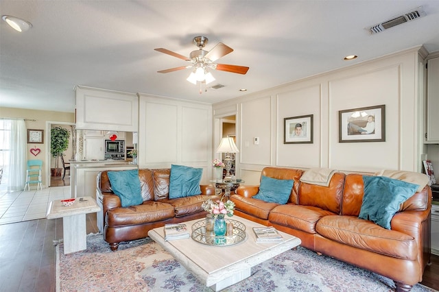 living room with ceiling fan, visible vents, a decorative wall, and wood finished floors