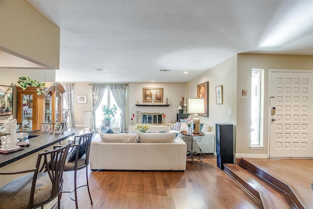 living area with a brick fireplace, a textured ceiling, baseboards, and wood finished floors