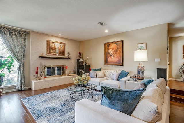 living area featuring recessed lighting, visible vents, a brick fireplace, a textured ceiling, and wood finished floors