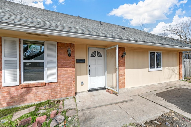 property entrance featuring brick siding and a shingled roof