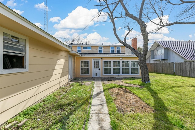 back of property with a lawn, a chimney, and fence