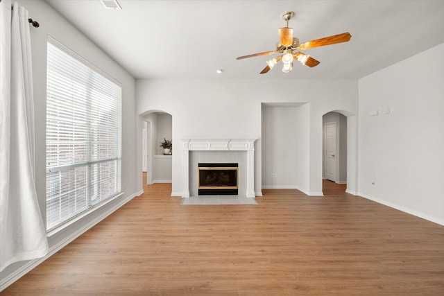 unfurnished living room with arched walkways, ceiling fan, baseboards, light wood-style floors, and a tiled fireplace