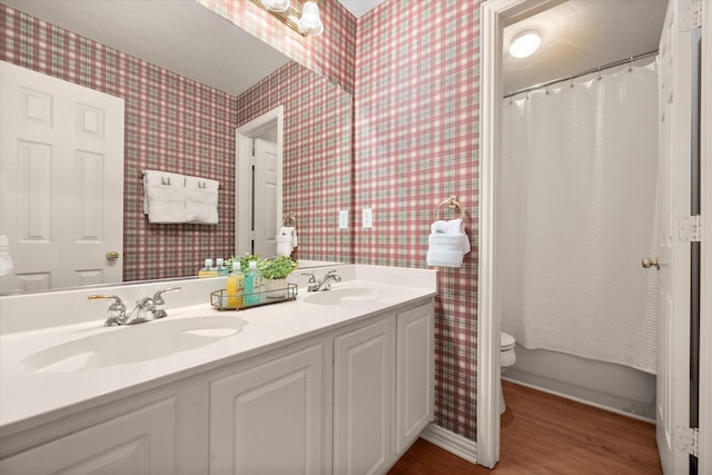 bathroom with wood finished floors, a sink, toilet, and wallpapered walls